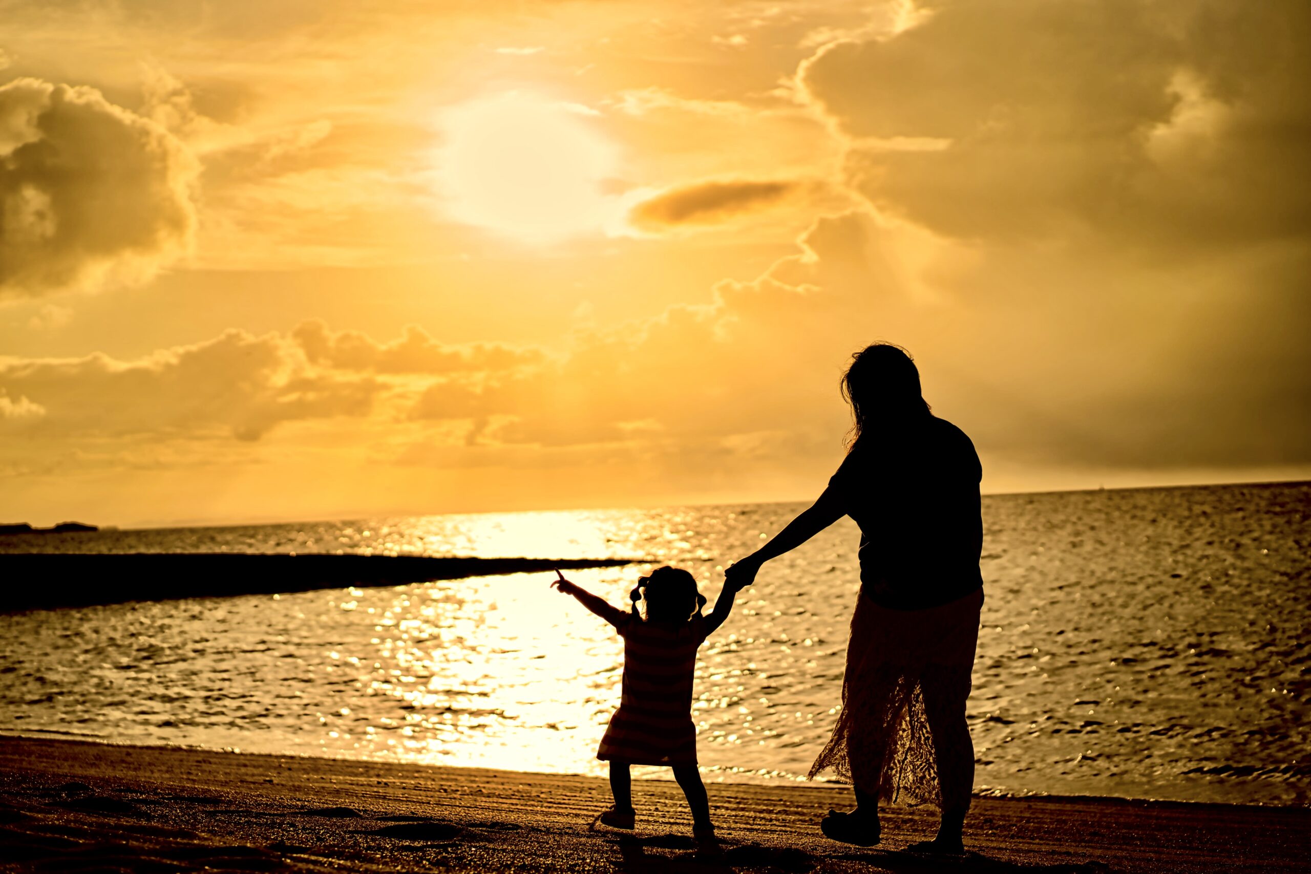 サンセットの日に子供と一緒にビーチを散歩する妊婦