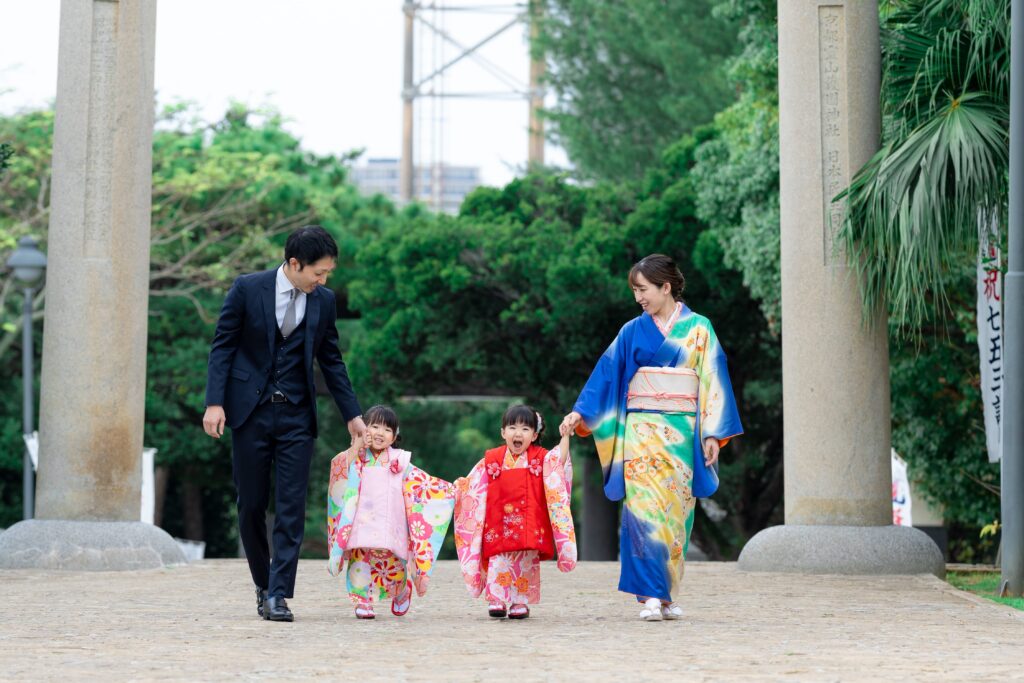 両親と手をつなぎ歩く双子の女の子の七五三記念写真(沖縄・護国神社)