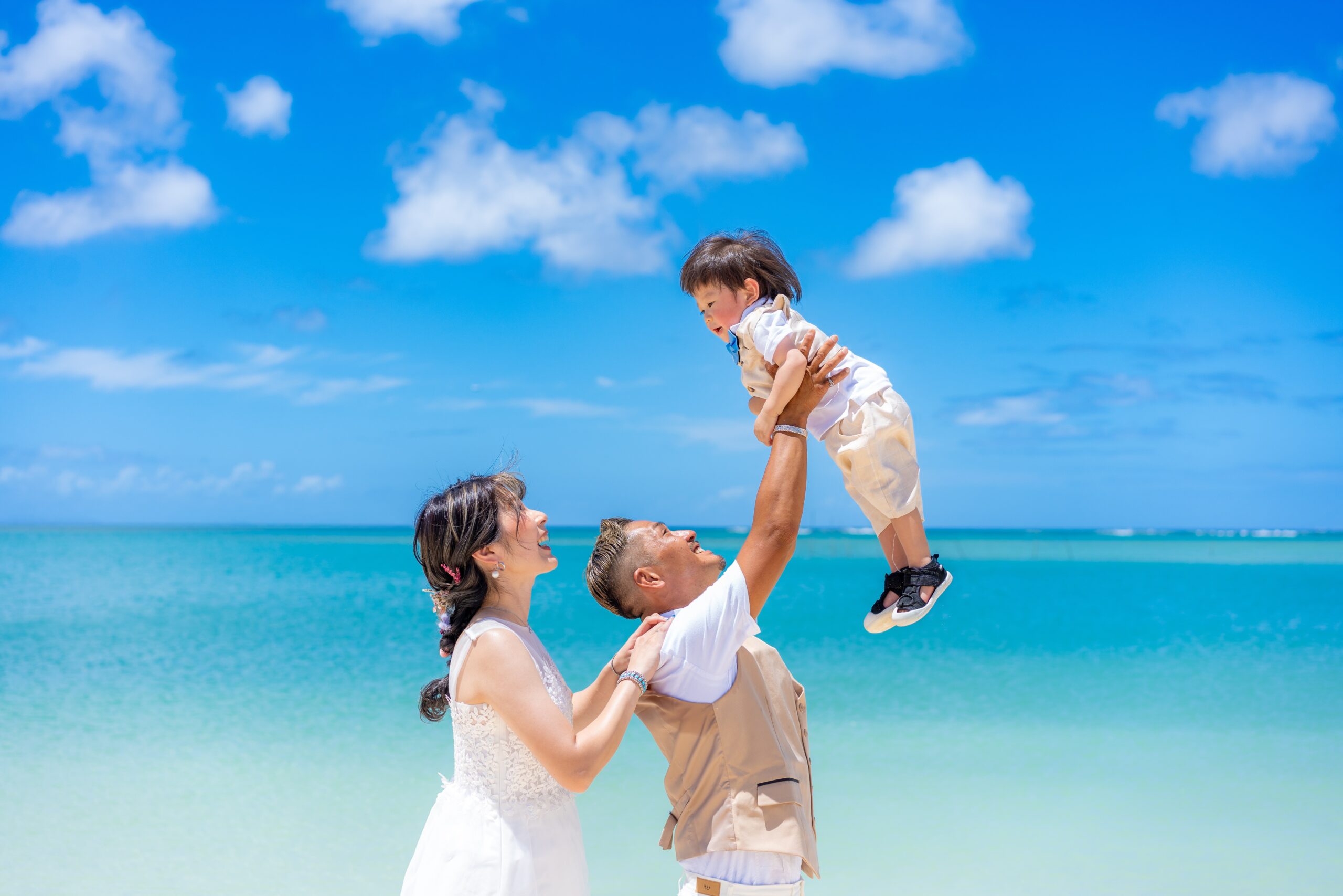 沖縄の海をバックに子どもを抱き上げるウェディングファミリーフォト