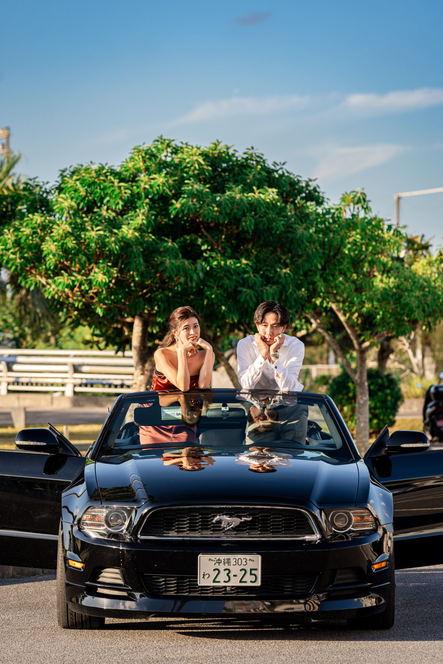 緑豊かなガジュマルの木の前で車と新郎新婦