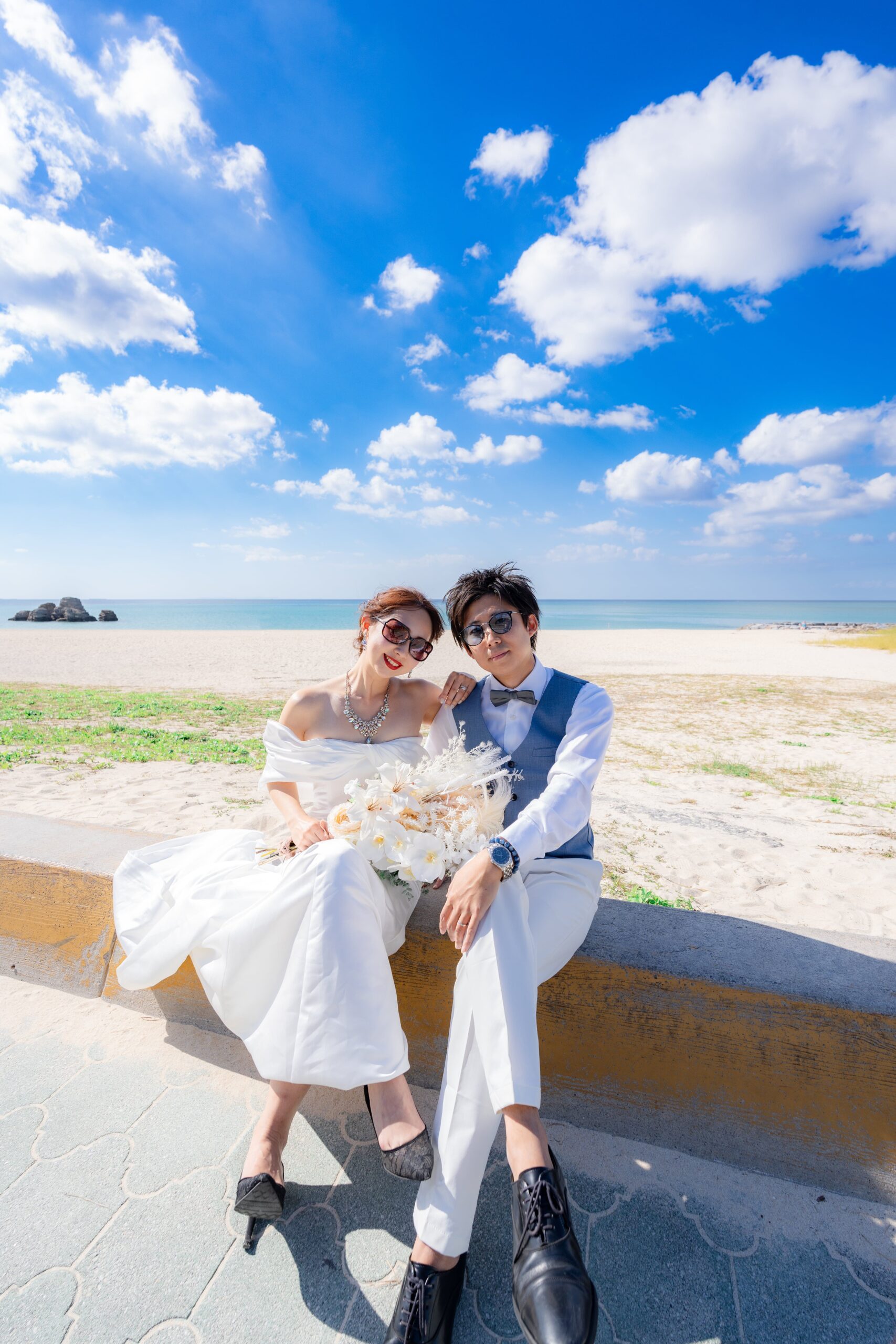 ヤシの木と青空の下でウェディングドレス姿の新婦とタキシードの新郎