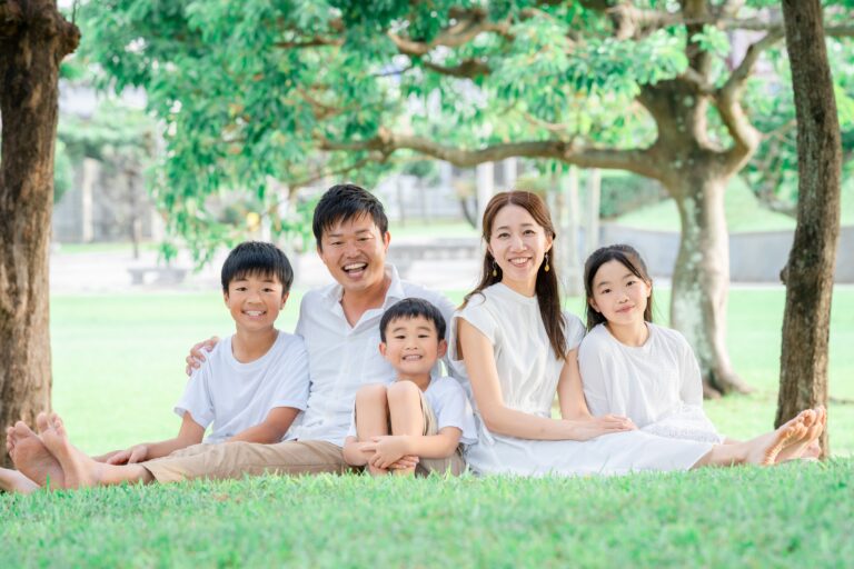 沖縄の緑をバックに家族全員がカメラ目線で笑顔のロケーションフォト｜沖縄ファミリーフォトビーチ