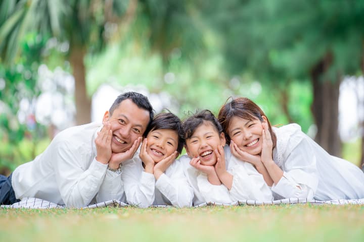 芝生の上で笑顔を並べる家族写真