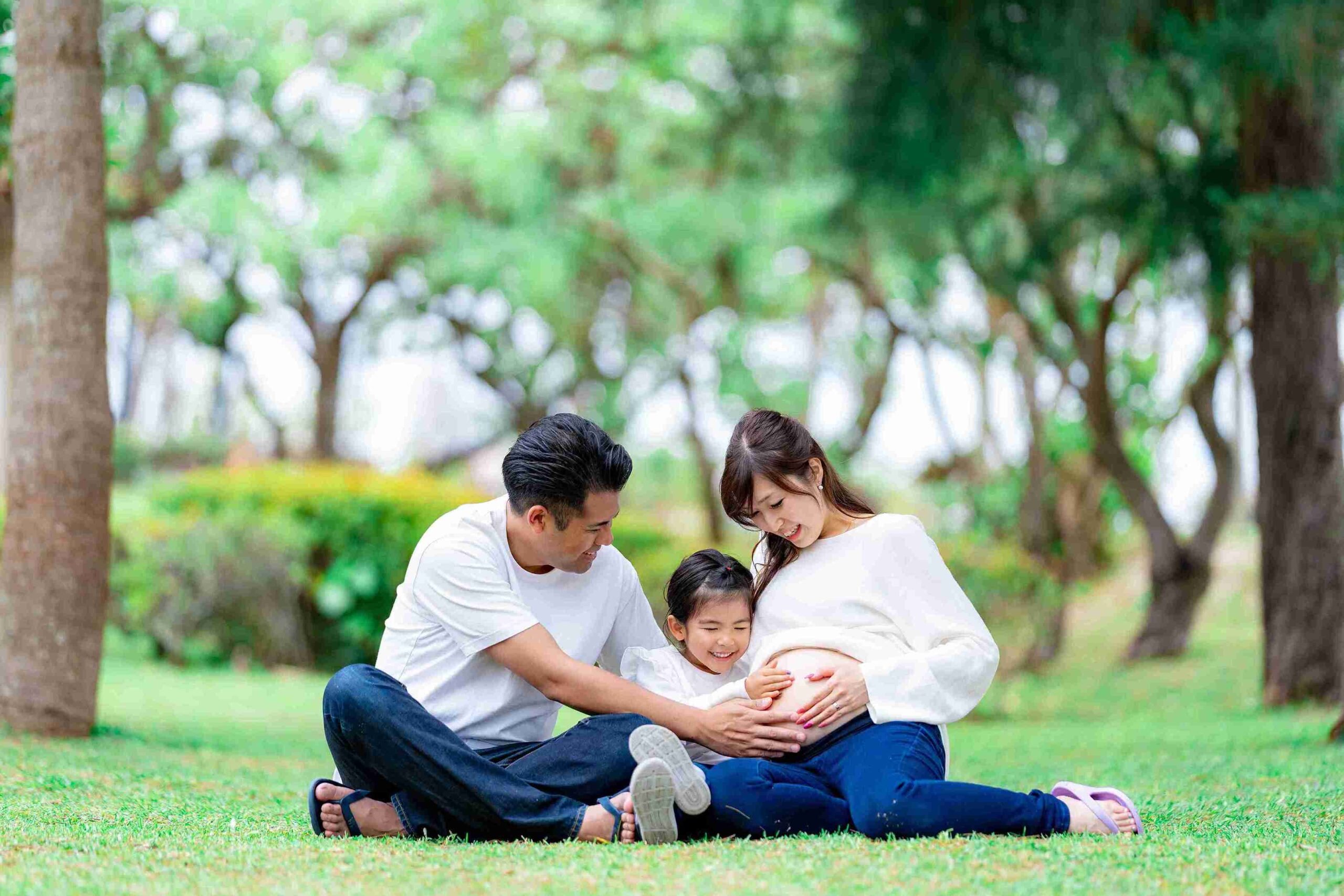 沖縄の豊かな自然の中で撮影した家族のマタニティフォト。パパと上の子がママのお腹に手を当てる温かいワンシーン。
