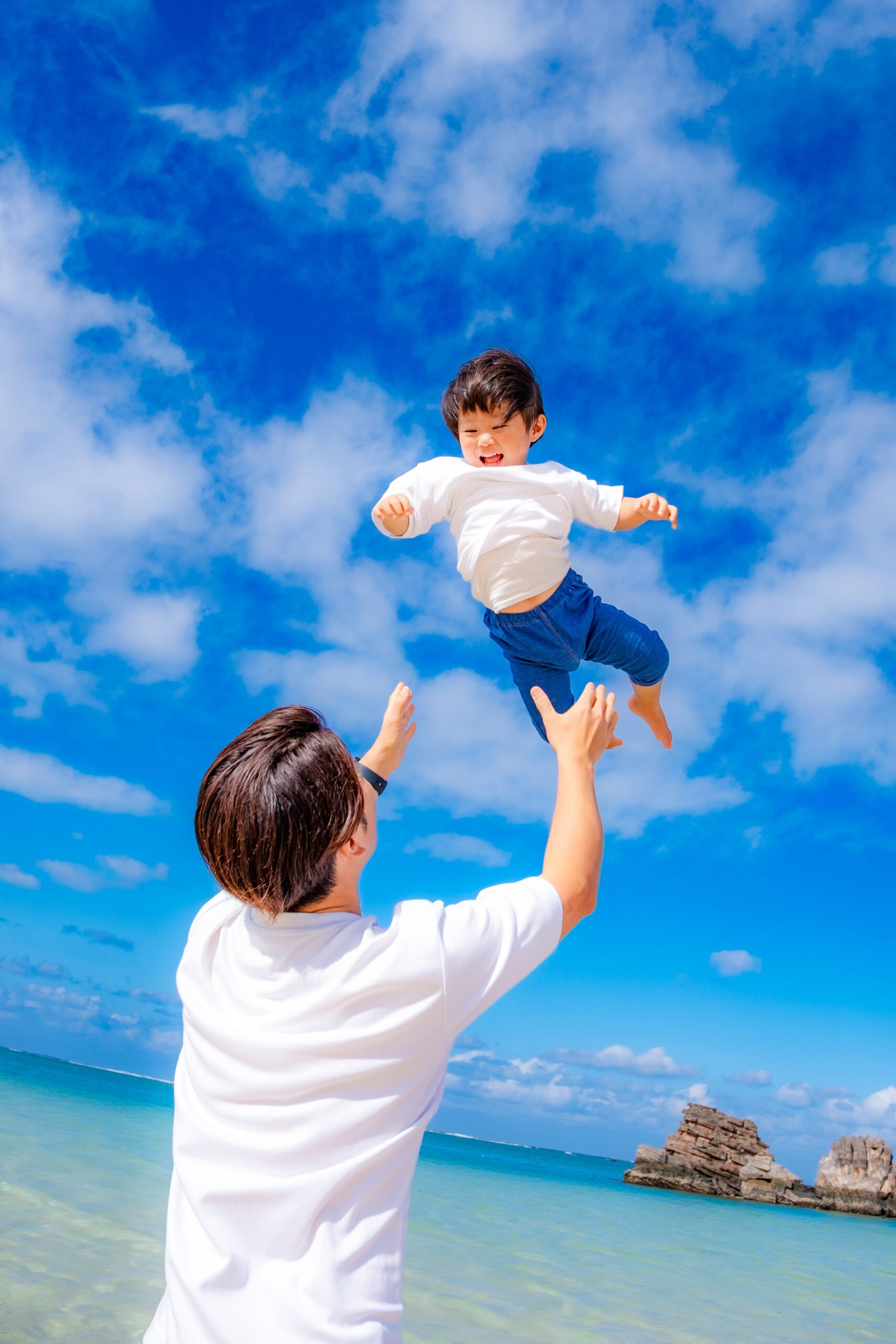 沖縄の海で父親に高い高いされて笑顔の子どもの家族写真｜沖縄出張撮影