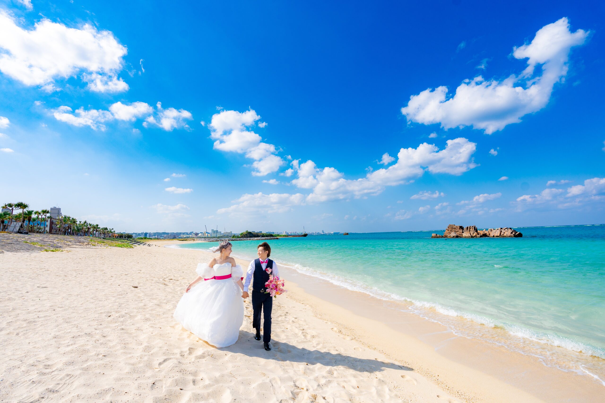 青い海と空を背景に新郎が新婦を抱き上げるウェディングフォト