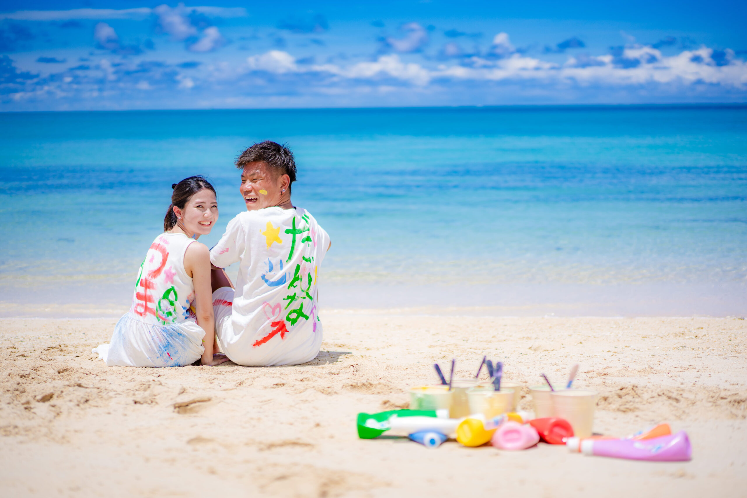 沖縄ペイントフォト｜沖縄の海をバックに絵の具まみれカップルの後ろ姿ショット