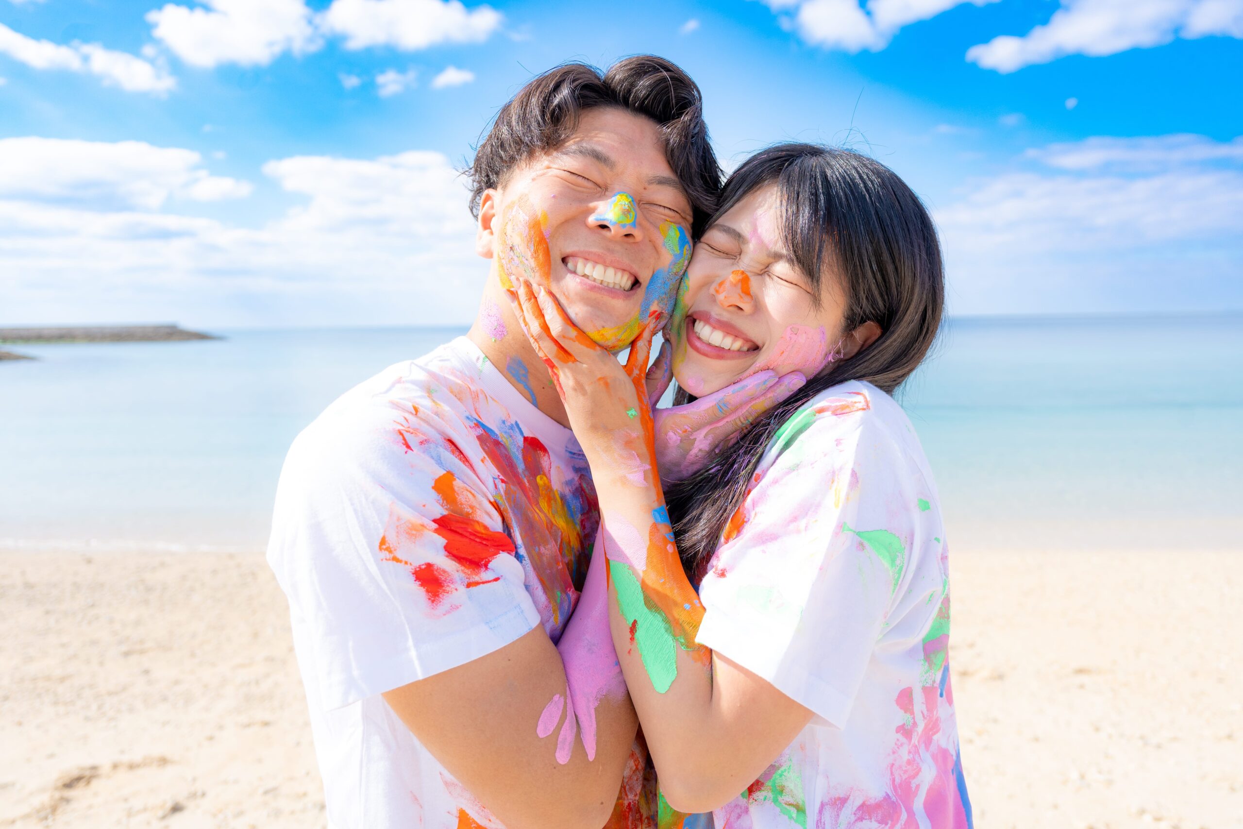 沖縄ペイントフォト｜仲良しポーズで絵の具まみれのカップル記念日ビーチ撮影