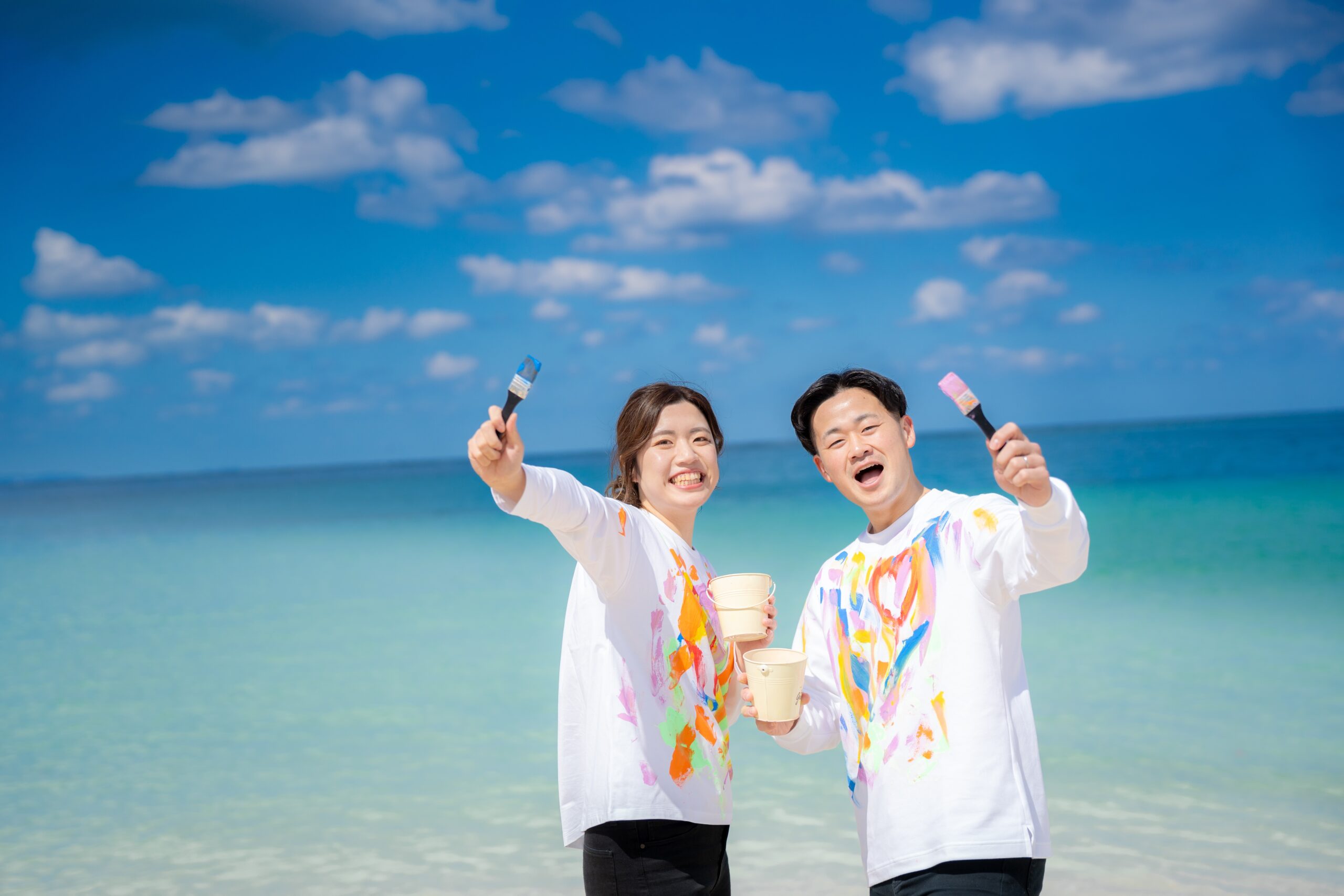 沖縄ペイントフォト｜青い海をバックに絵の具まみれのカップルがカメラ目線で撮影
