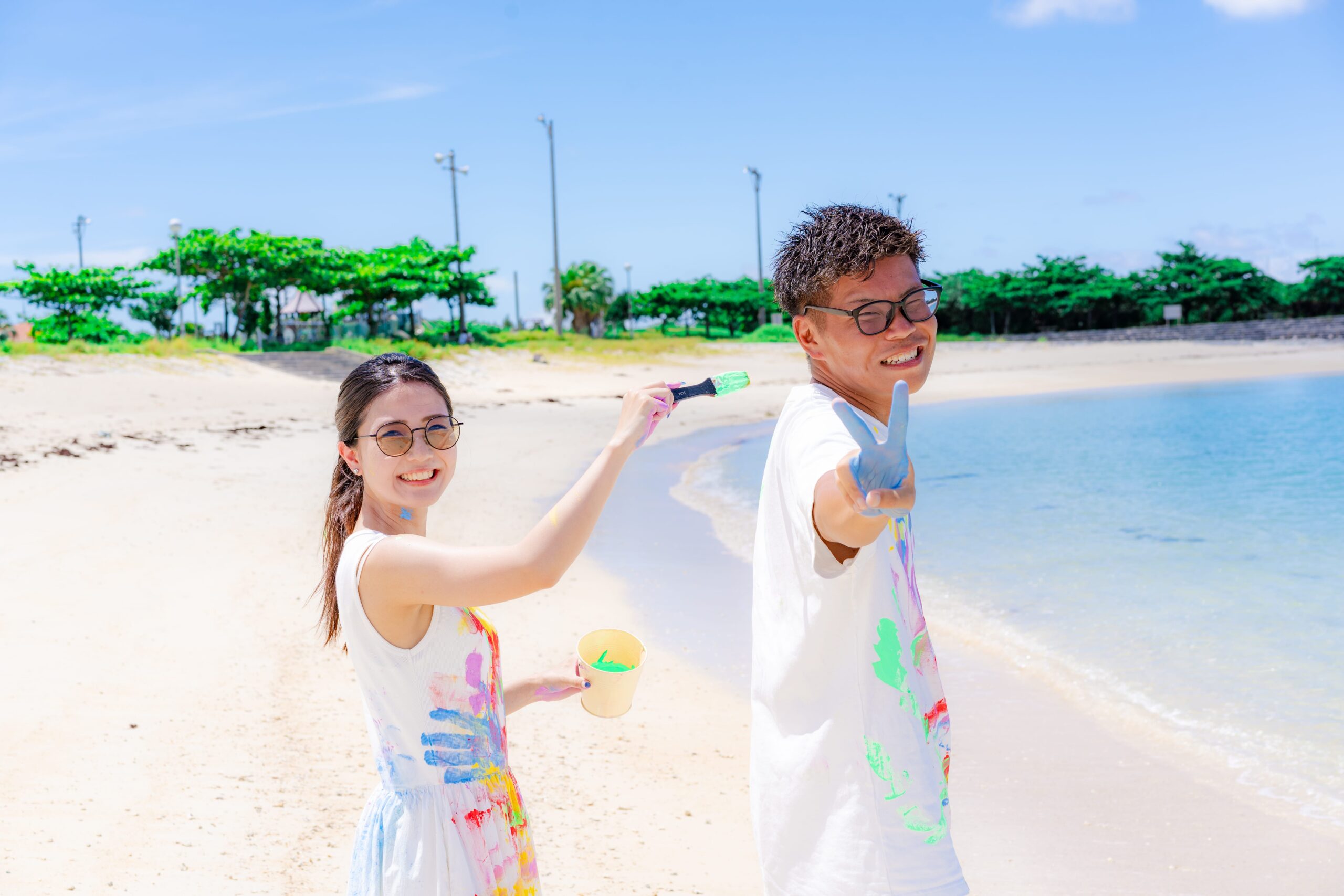 沖縄ペイントフォト｜ビーチで絵の具まみれのカップルがカメラ目線で笑顔の記念撮影