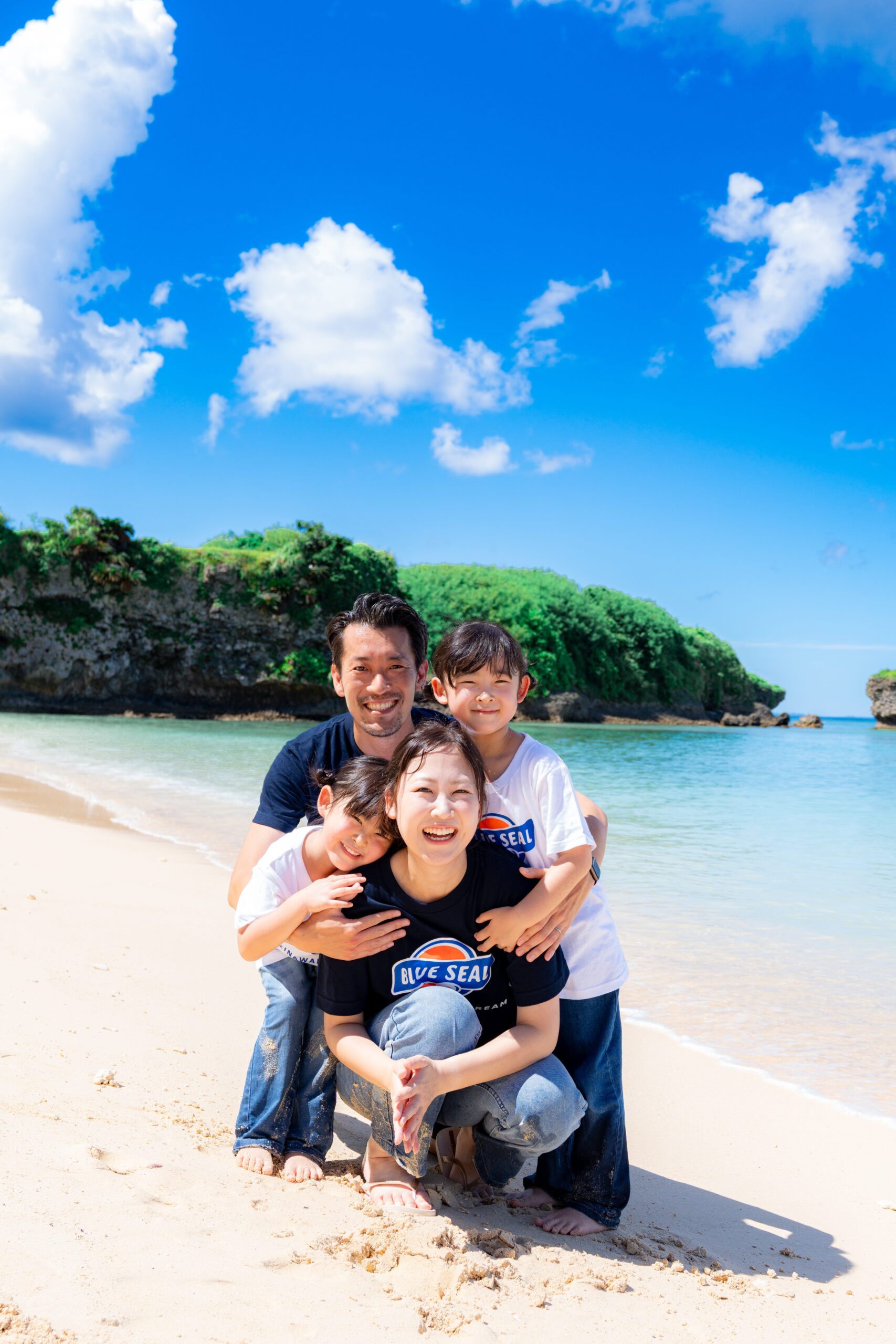 沖縄の海をバックに家族みんなでぎゅっとハグするロケーションフォト｜沖縄ファミリーフォト