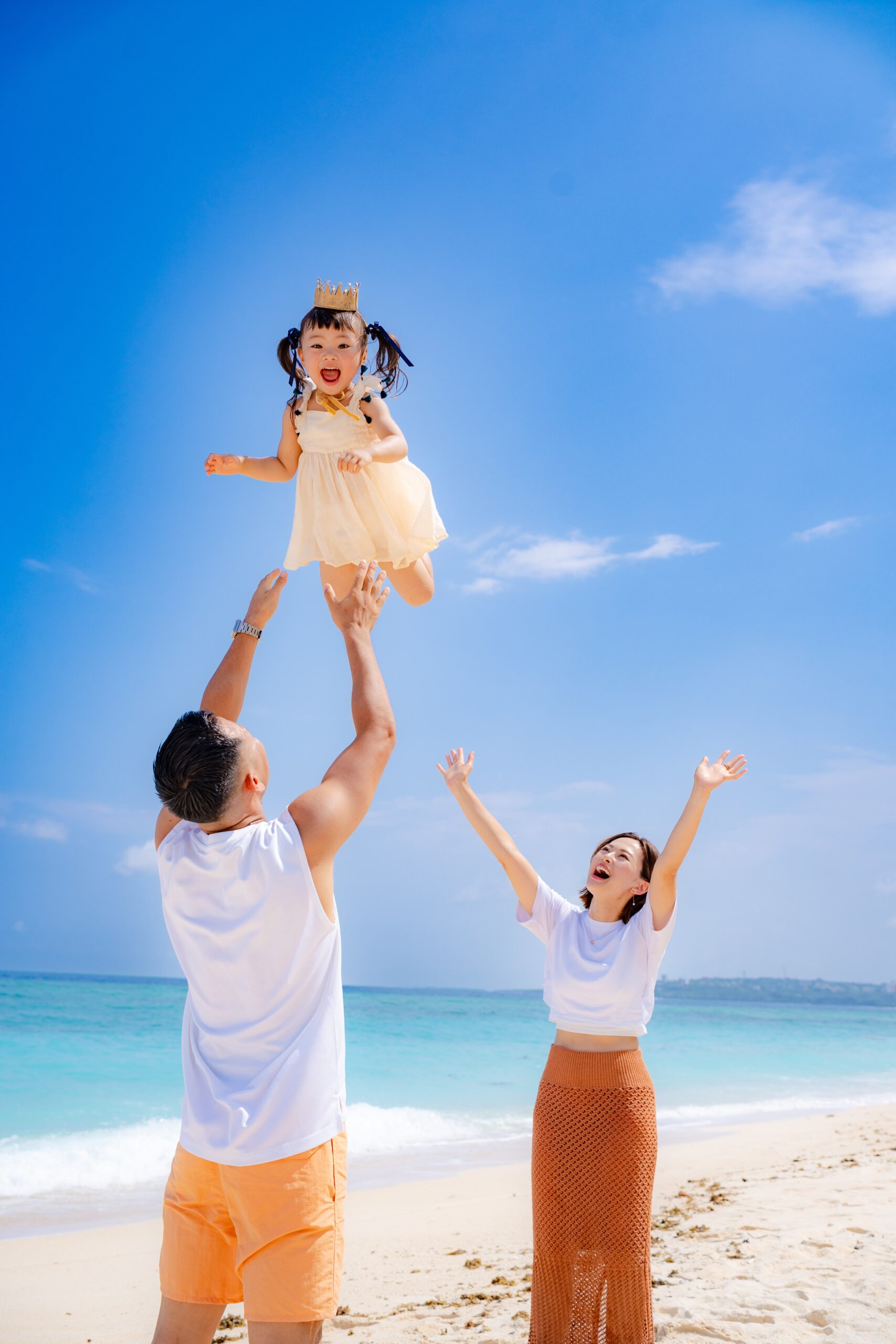 沖縄のビーチで誕生日の主役が高い高いされる笑顔の家族写真｜沖縄ファミリーフォト