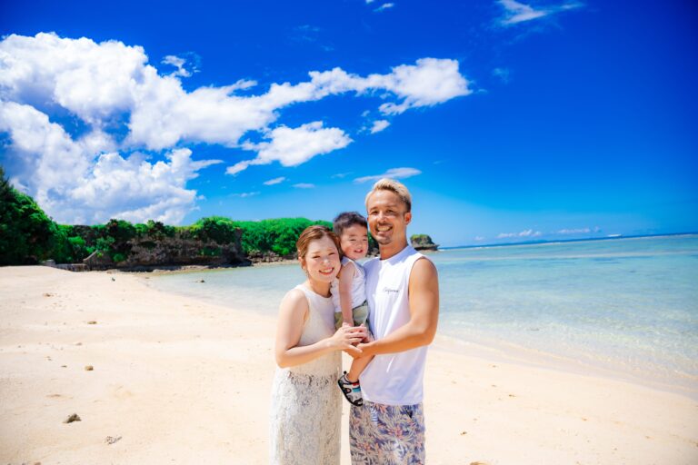沖縄の透き通る海をバックに家族3人がカメラ目線で笑顔のファミリーフォト｜沖縄家族写真ビーチ