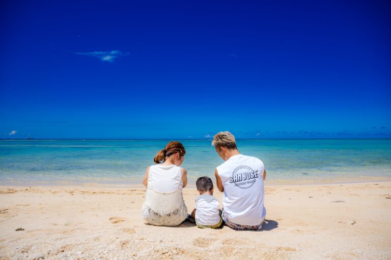 沖縄の海をバックに家族3人でおすわりする温かいファミリーフォト｜沖縄ファミリーフォトビーチ