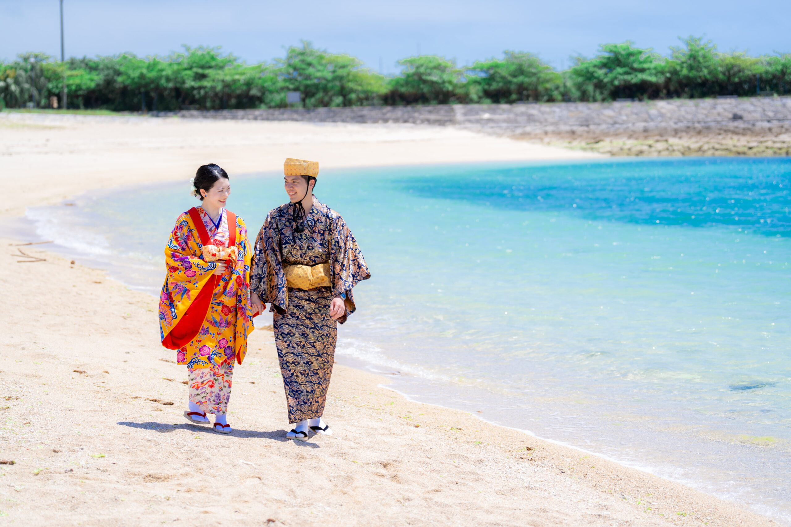 沖縄のビーチで琉装姿のカップルが手をつないで歩く