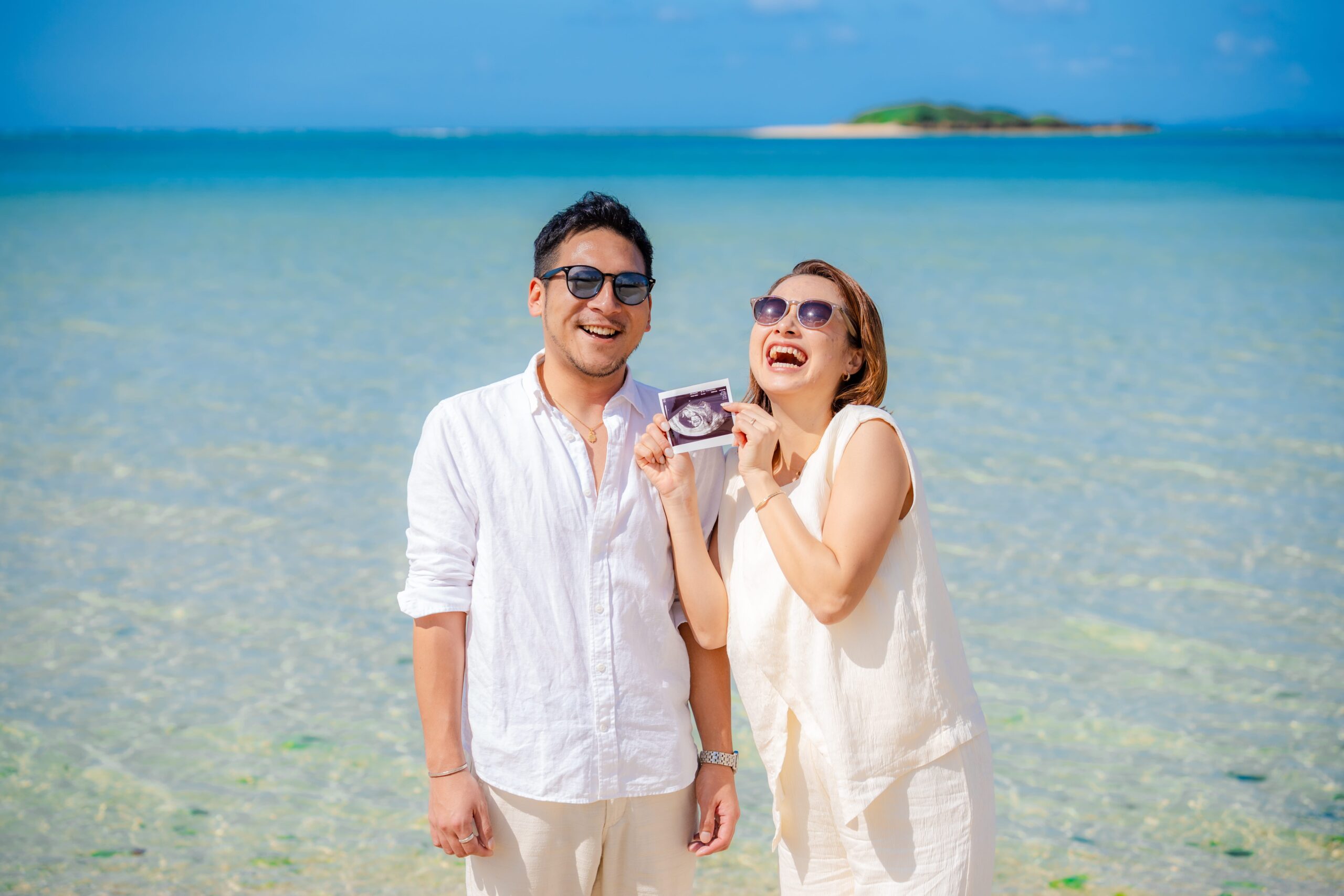 沖縄マタニティフォト｜最高の笑顔でエコー写真を見せる海辺の夫婦撮影